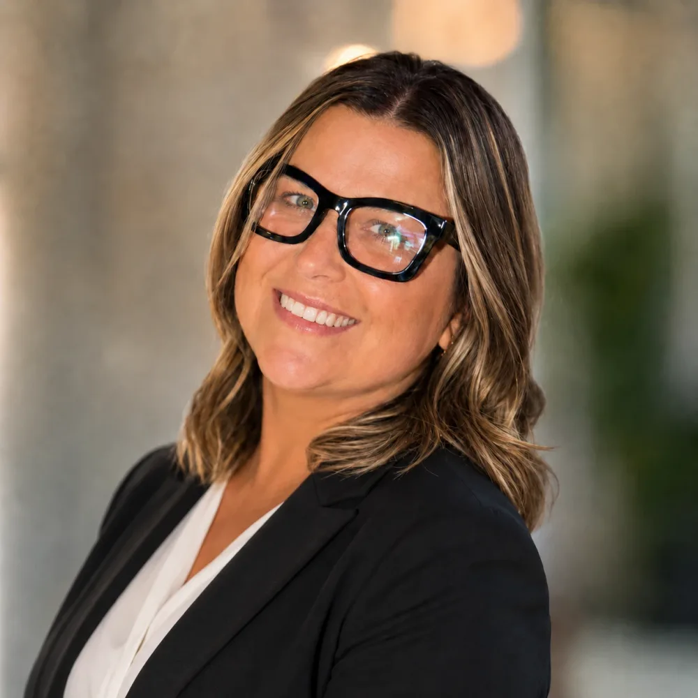 Joanna Karlicka, founder of Cherry Tree Solutions, smiling, with shoulder length highlighted hair, black rectangular glasses, a black blazer and a white blouse